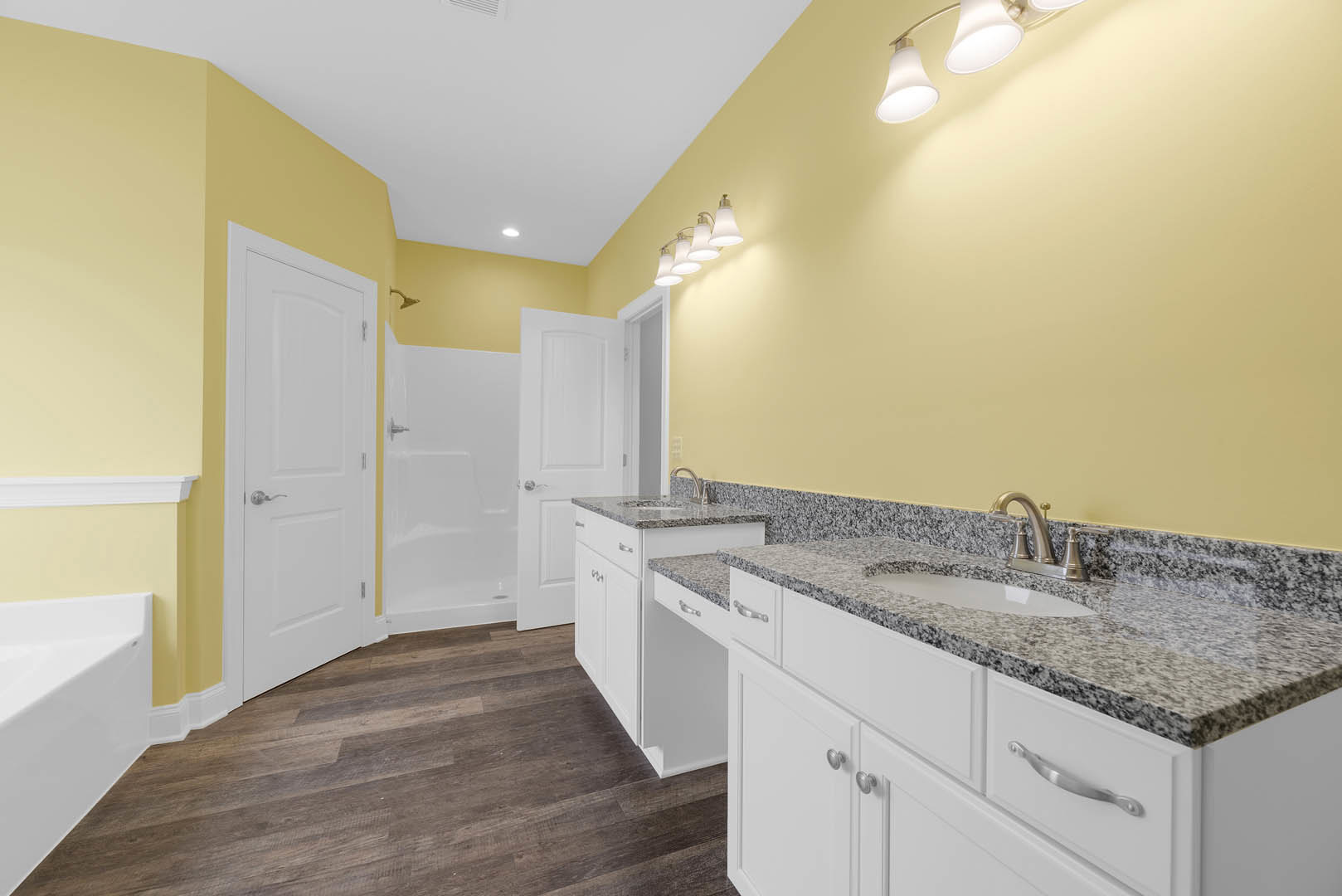 Bathroom featuring marble countertop, undermount sink with chrome faucet, white cabinetry, glass-enclosed shower with tile walls, and freestanding white bathtub.