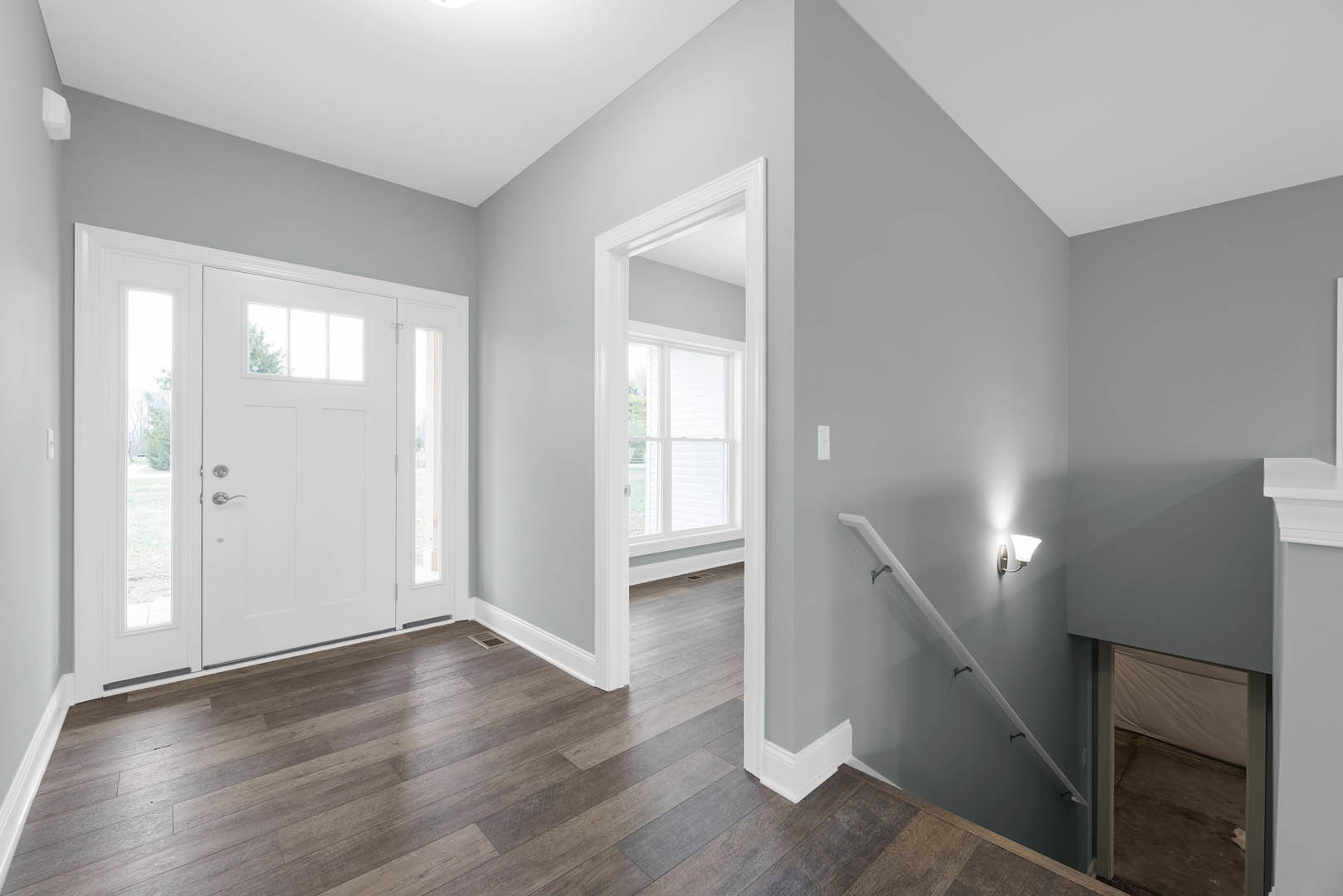 Hallway with wood flooring, white plaster walls, staircase with wooden steps and white railing, white door featuring glass window panes, wall-mounted light fixture