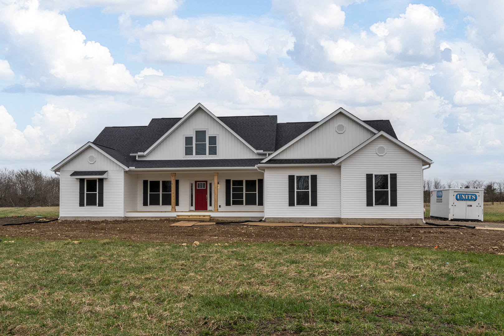 White siding house with red front door, black roof, white-framed windows, and green grass lawn under partly cloudy sky