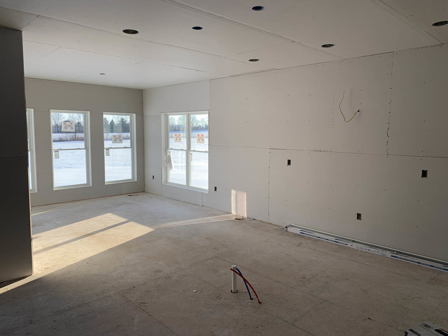 Room with plaster walls, large windows, concrete flooring, exposed pipes and wiring, and a black accent wall.