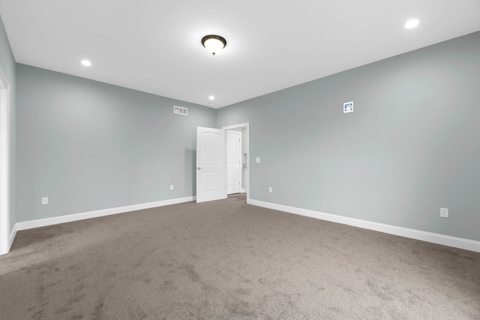 Carpeted room with white walls, white door featuring a silver handle, ceiling light fixture, and decorative molding along the ceiling.