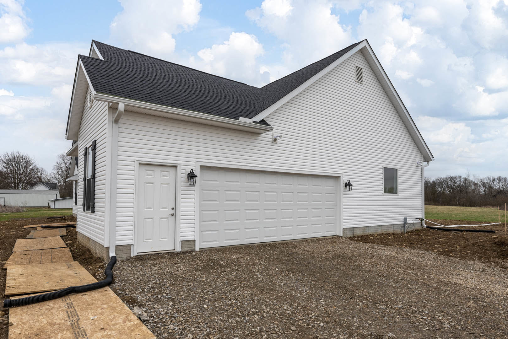 White siding house with attached garage, concrete driveway, white framed windows, and gable roof under partly cloudy sky.