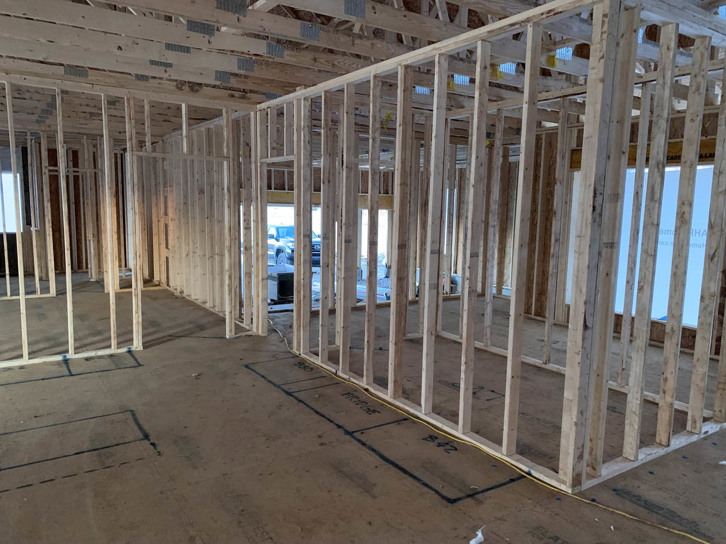 Exposed wood framing in an unfinished room with concrete floor and black construction markings