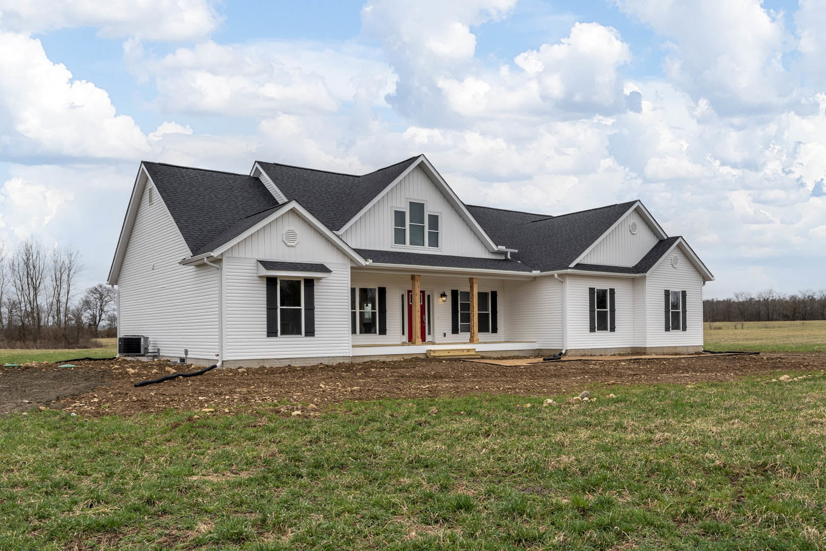 White house with black shutters and large grassy lawn, Southfork Ranch visible in the background, scattered trees and partly cloudy sky