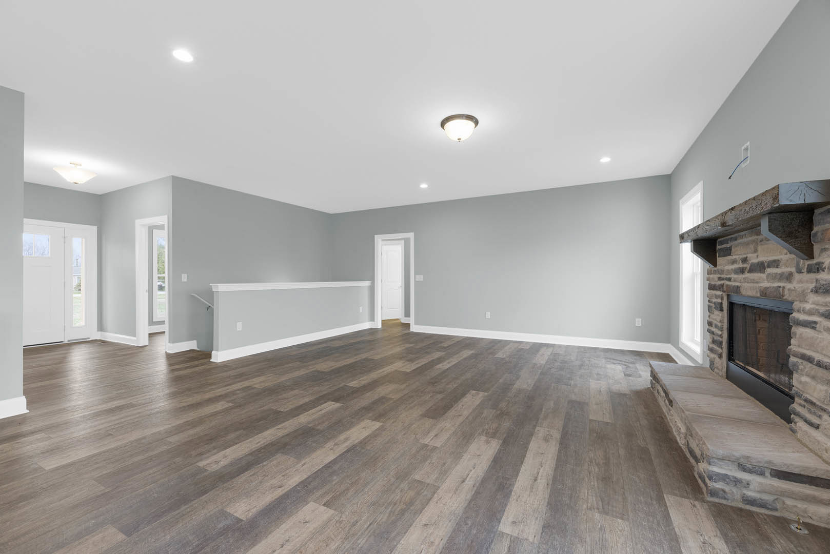 Wood flooring and white walls with white trim, ceiling-mounted light fixture, white door with window, fireplace along one wall