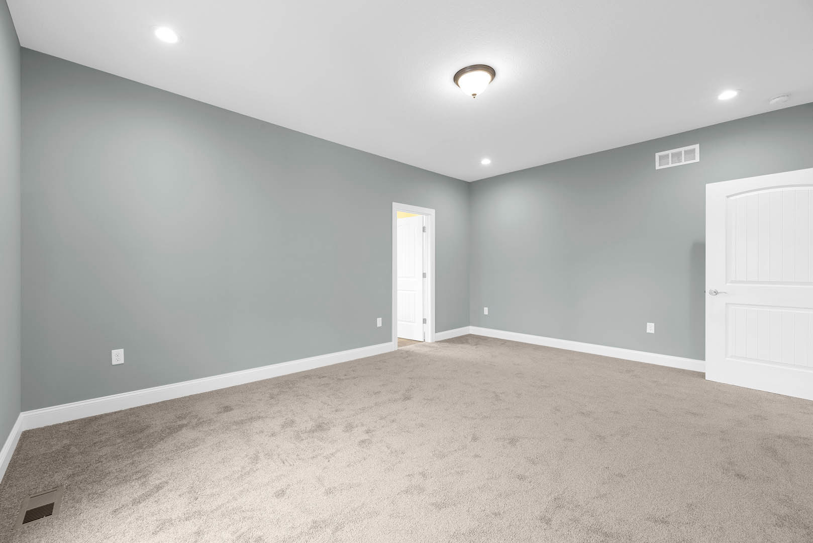 Carpeted bedroom with white door open, white wall vent, and ceiling light fixture