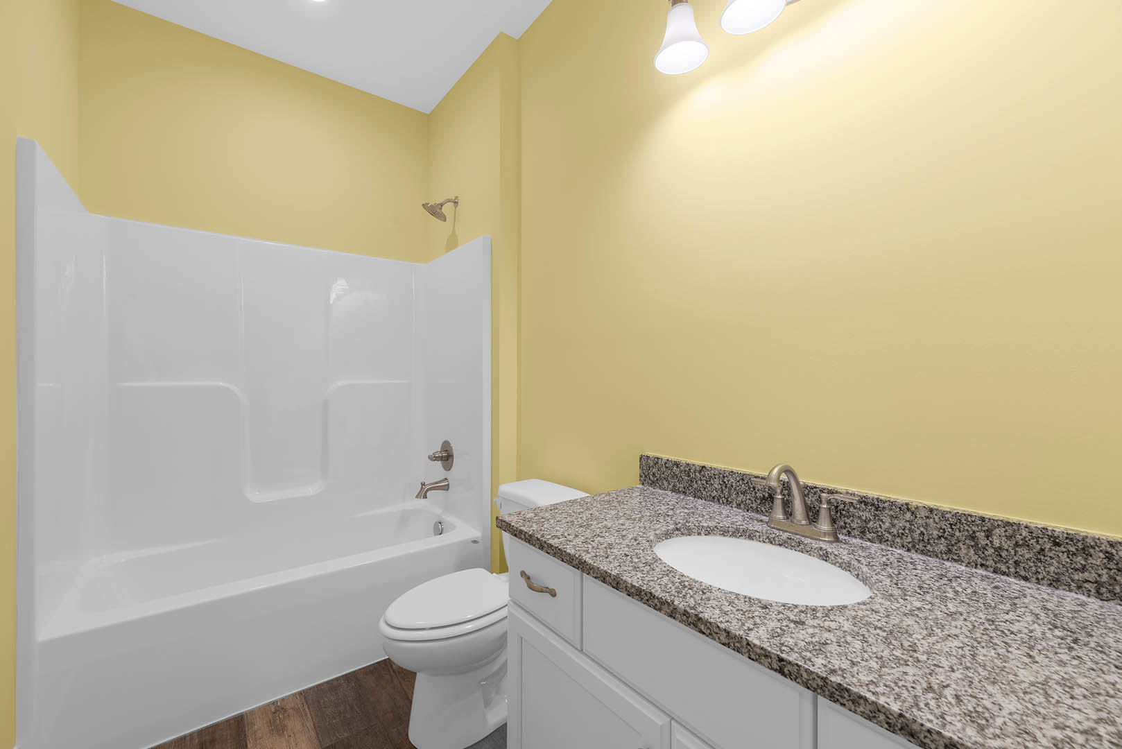 Bathroom with white bathtub, white toilet, and white sink featuring a black and white speckled countertop; light tile flooring and neutral wall tiles; chrome faucet and plumbing