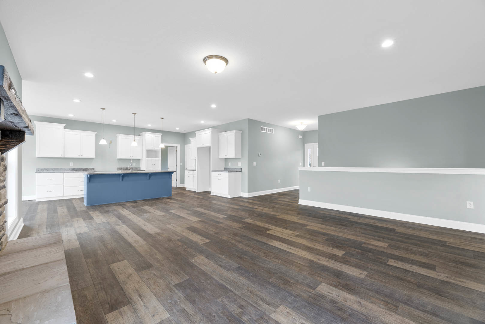 Open-concept kitchen with wood flooring, white walls, blue accent wall, white cabinetry, and modern ceiling light fixture