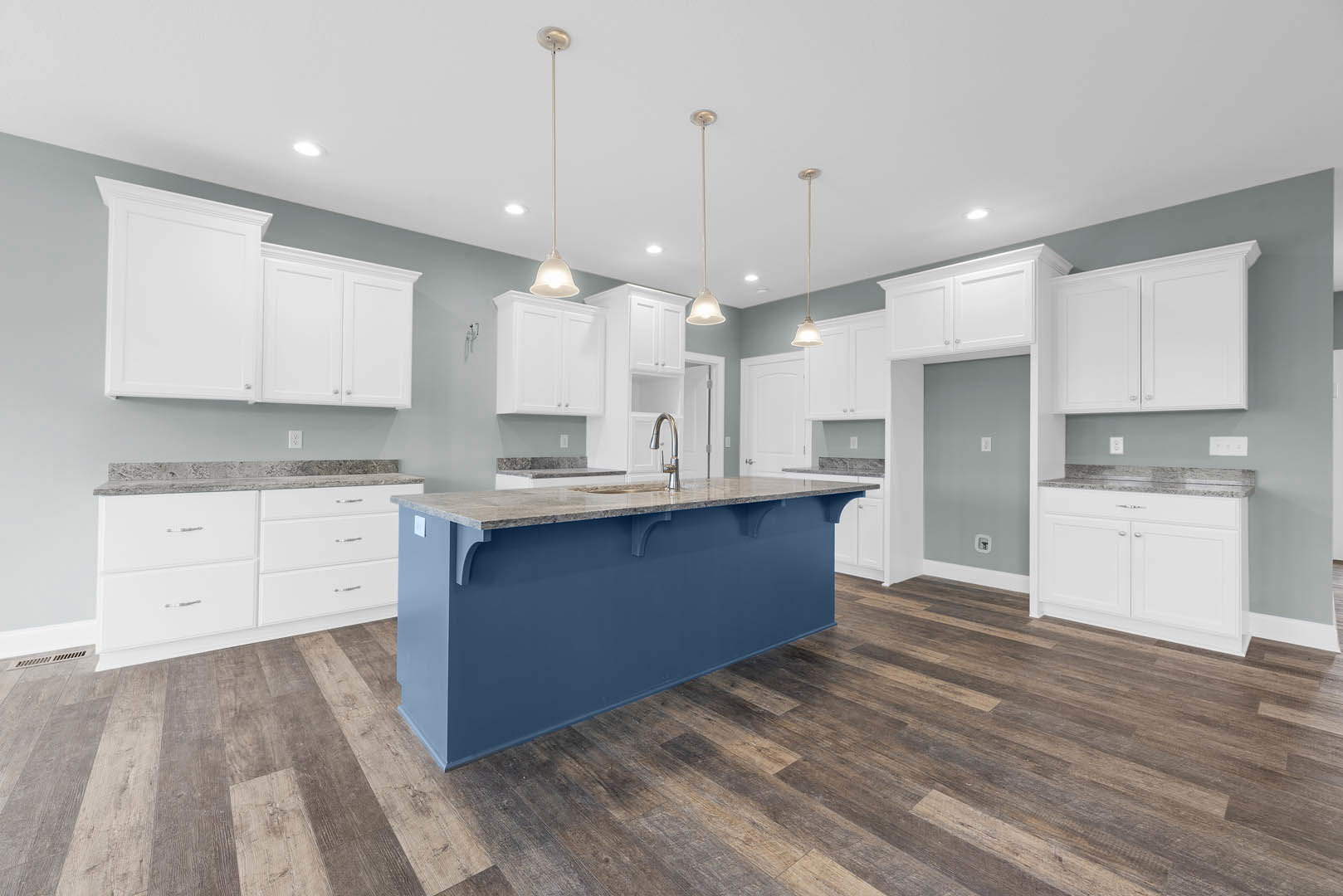 Blue kitchen island with marble countertop, white cabinetry and drawers, wood flooring, white pole, and black flag in a bright, modern kitchen interior.