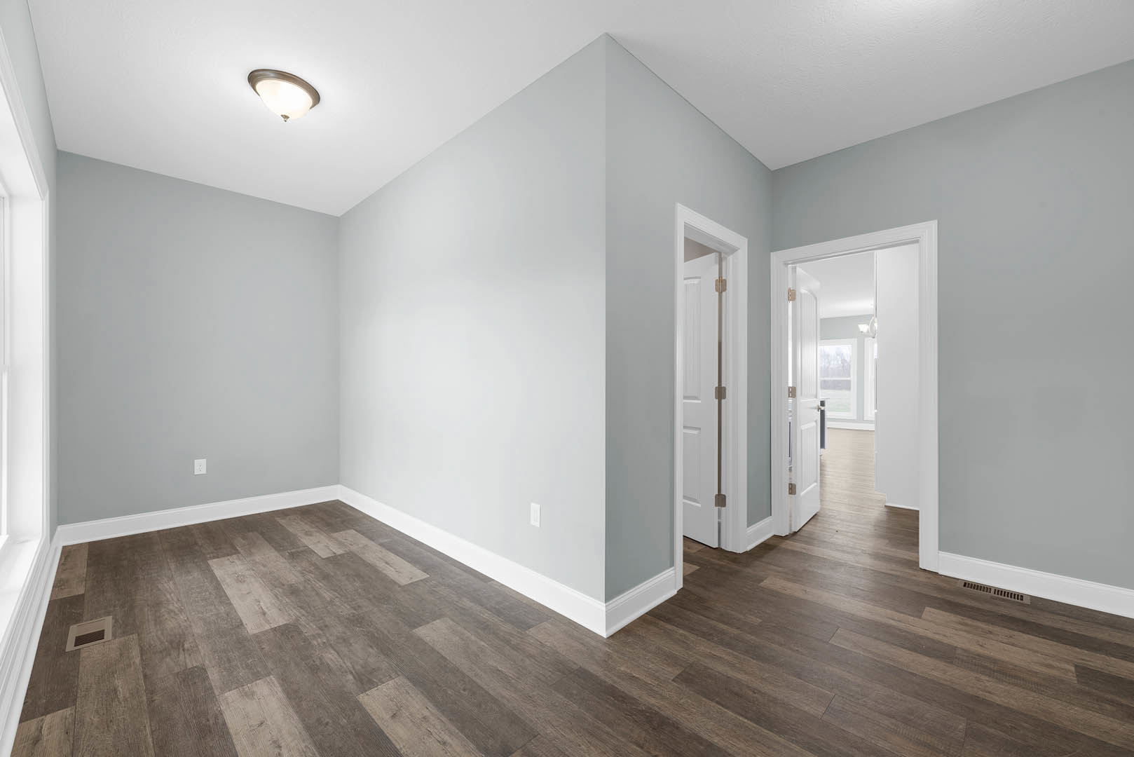 White walls, wood flooring, ceiling light fixture, white door with metal bar, wall vent