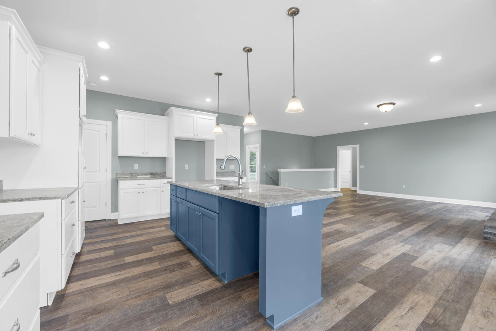 Kitchen with white shaker cabinets, central island featuring built-in sink, stainless steel appliances, light stone countertops, hardwood flooring, and recessed lighting