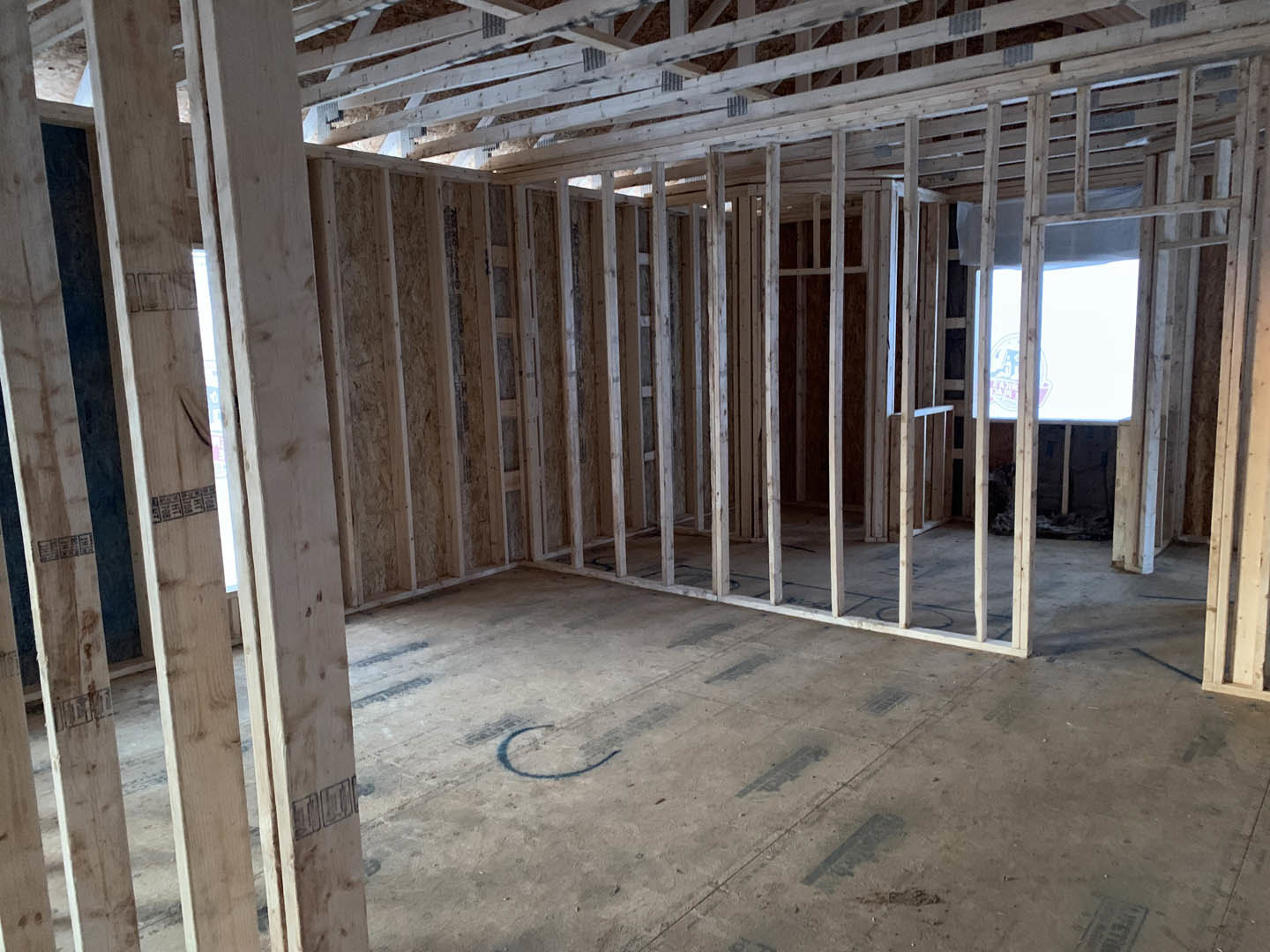 Room under construction with exposed wood framing, concrete floor, and window opening; insulation visible between beams.