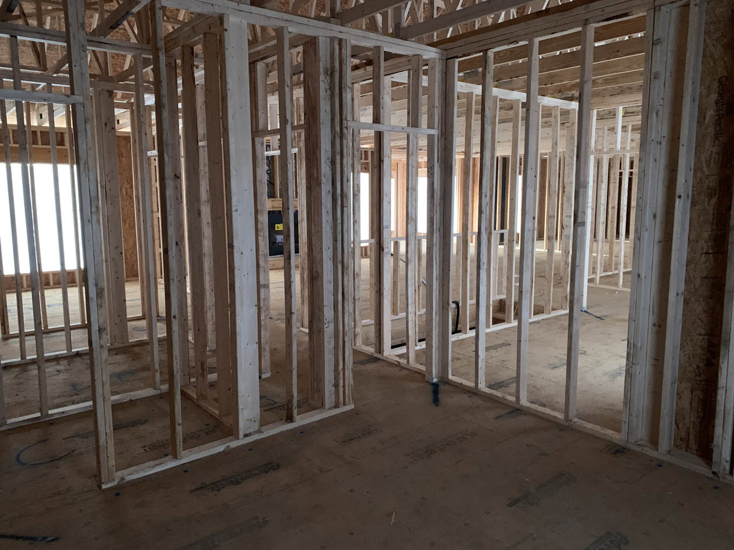 Wood-framed room under construction with exposed beams, concrete floor, and large window opening