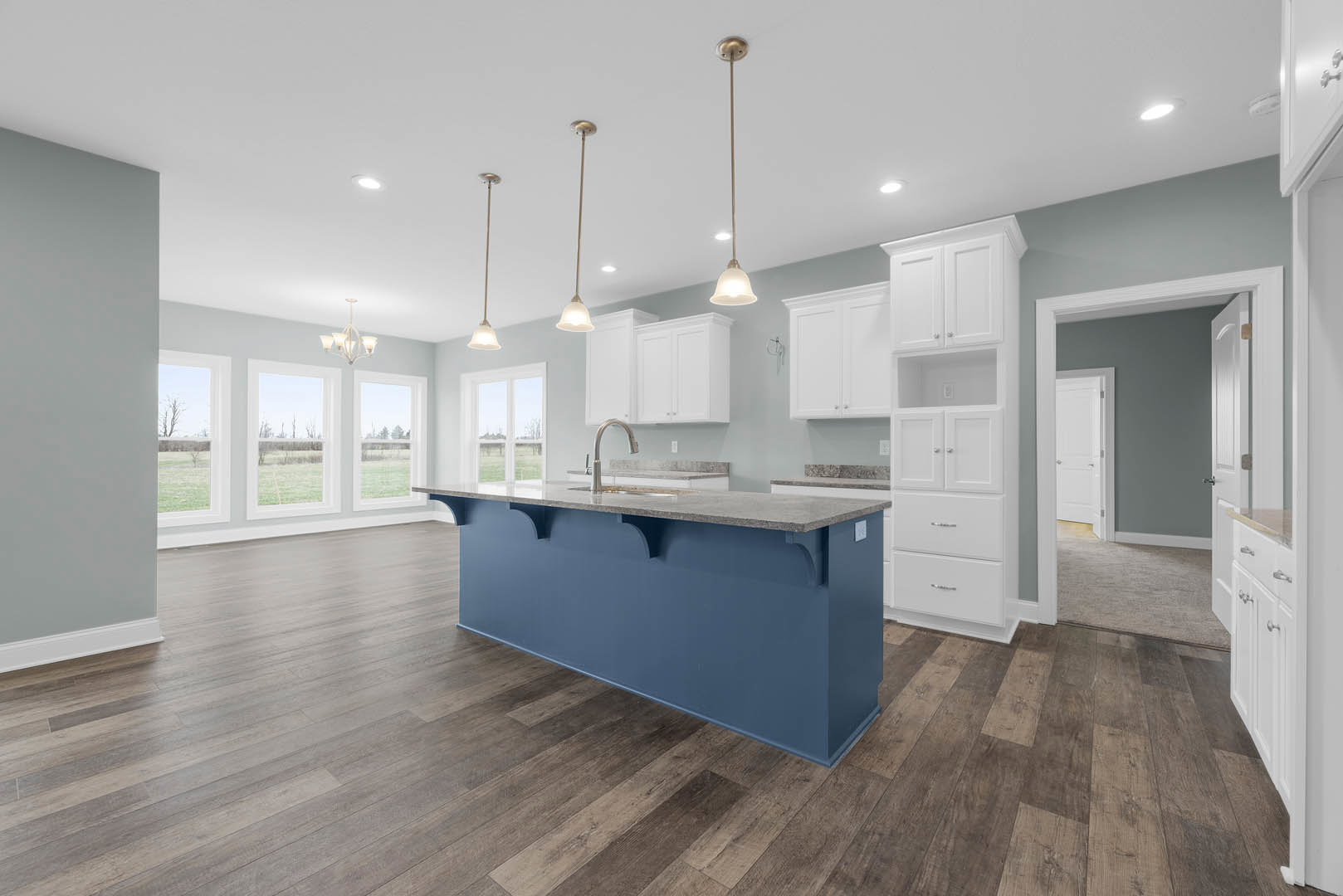 Blue kitchen island with white shaker cabinets, wood flooring, white quartz countertops, stainless steel sink, and open shelving against a blue accent wall.