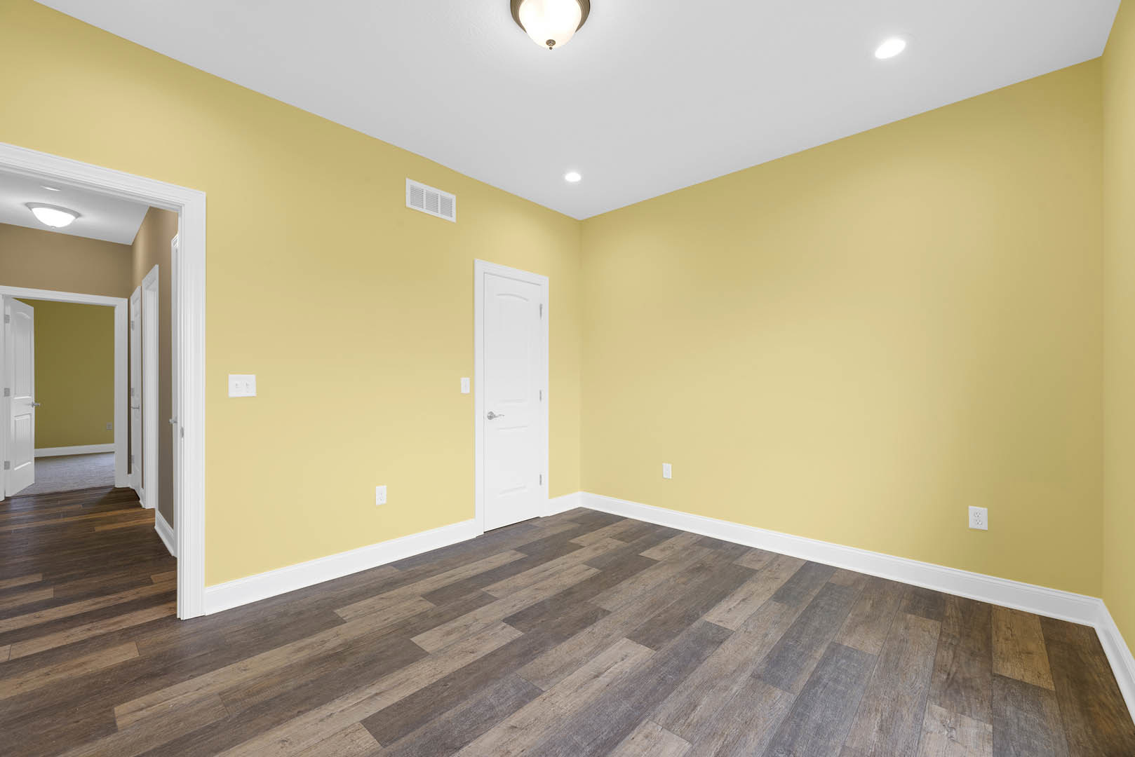 Yellow walls, wood laminate flooring, white door with silver handle, ceiling light fixture, wall vent, white base molding