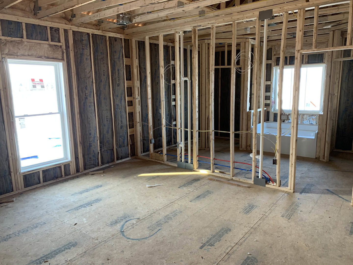Bathroom under construction with exposed wooden ceiling beams, freestanding bathtub, unfinished flooring, and window displaying a sign.