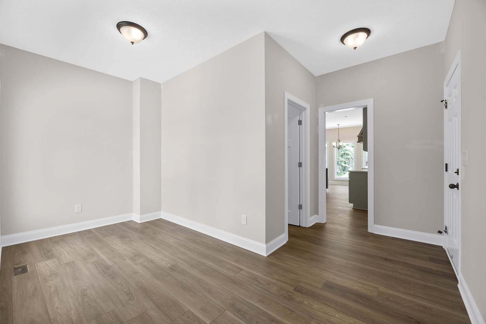 Wood flooring in a room with white plaster walls, a white door with visible hinge, and a modern ceiling light fixture.