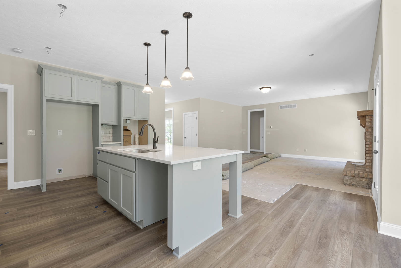 Kitchen with light wood flooring, central island featuring built-in sink, white cabinetry, white brick accent wall with light switch, white door with black handle, and laminate