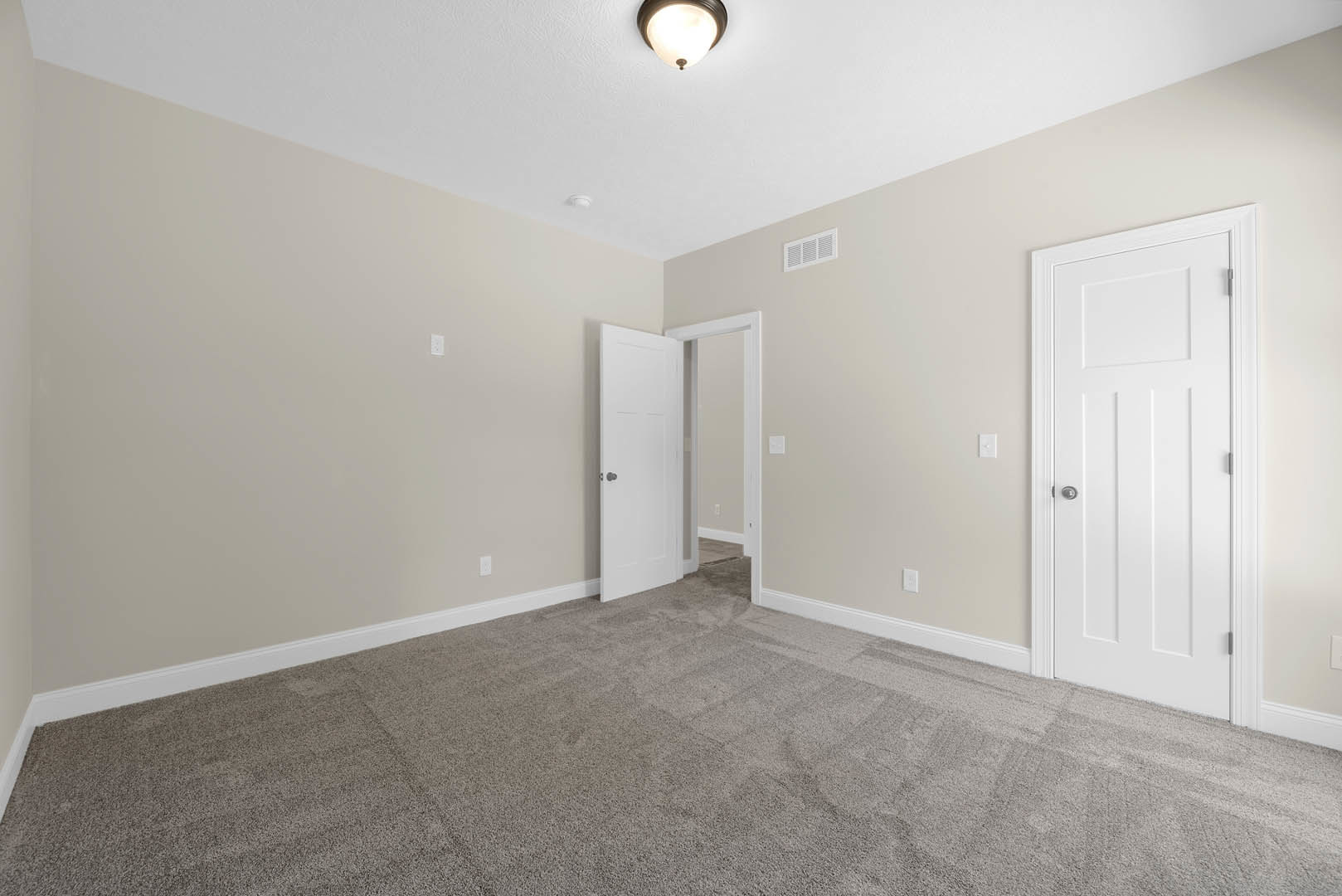 Carpeted bedroom with white door open, silver door knob, wall vent, and ceiling light fixture
