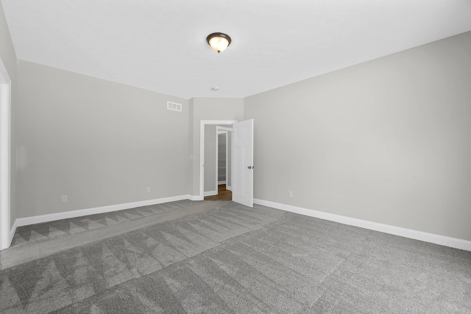 White door with black handle open into carpeted room, grey carpet flooring, white walls, ceiling light fixture, crown molding along ceiling.