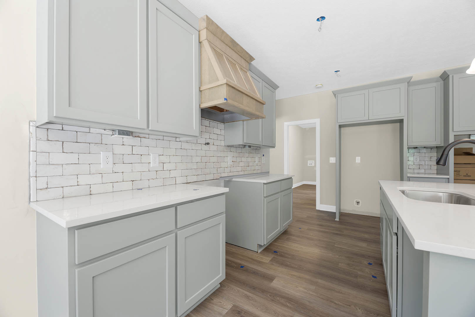 Kitchen with white shaker cabinets, wood plank flooring, white quartz countertops, stainless steel vent hood, and a white door with gold hinges