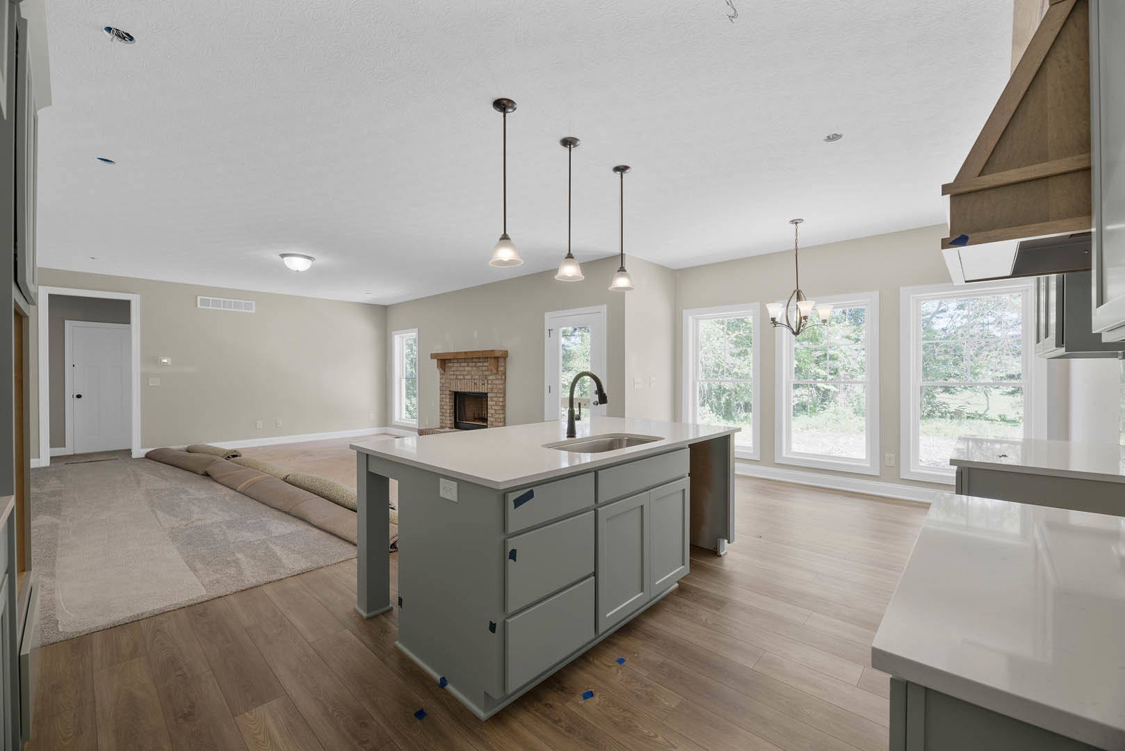 Spacious kitchen featuring a large central island with sink and drawers, patterned rug on wood flooring, white cabinetry, fireplace with wood mantle, and white door with black