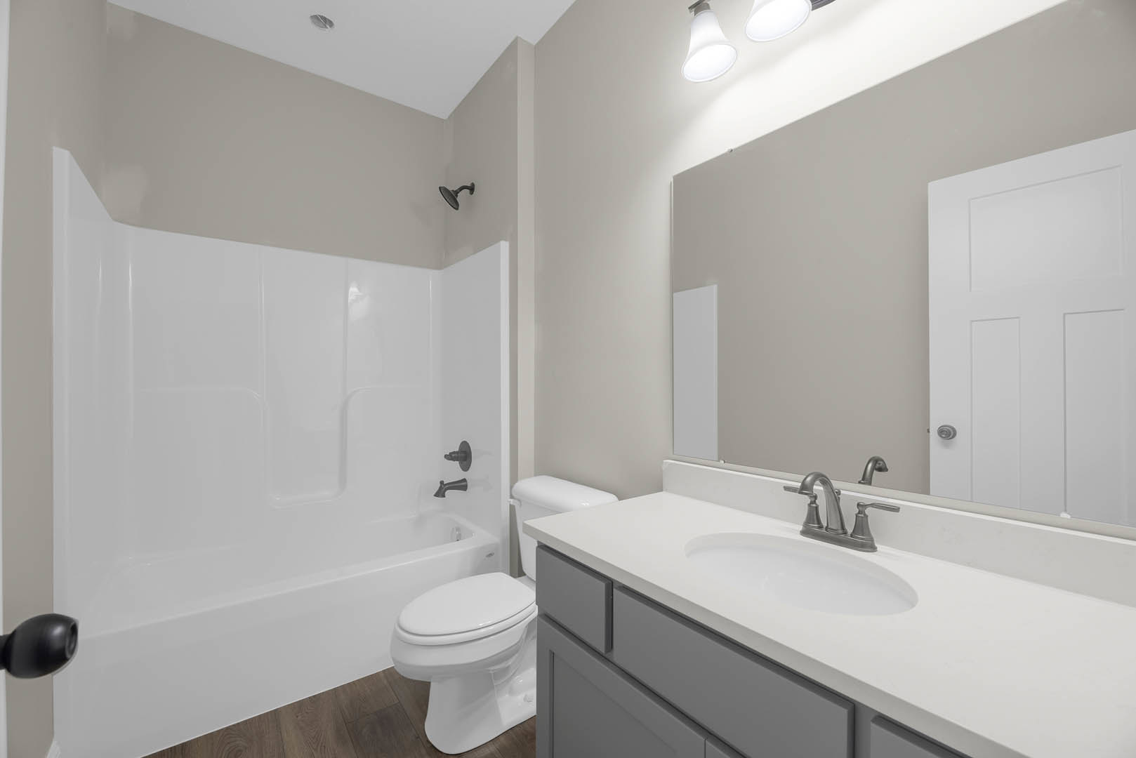 White bathtub and toilet beside a tiled wall, black shower head mounted above tub, white sink and silver-handled door visible in modern bathroom.