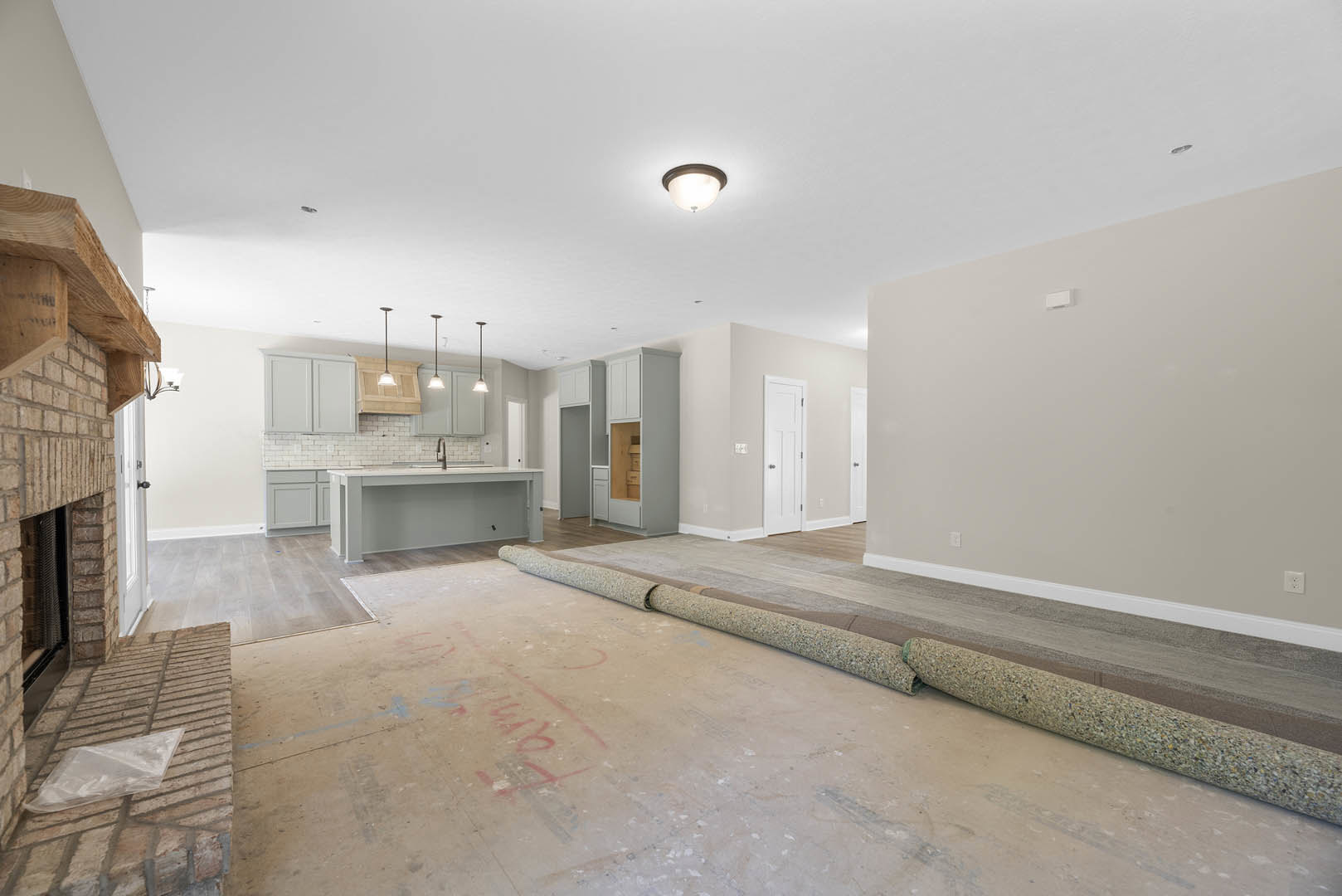 Wood-floored room with a roll of carpet, white table, ceiling light fixture, white door with silver knob, close-up of white cabinet, and shelving with storage boxes.