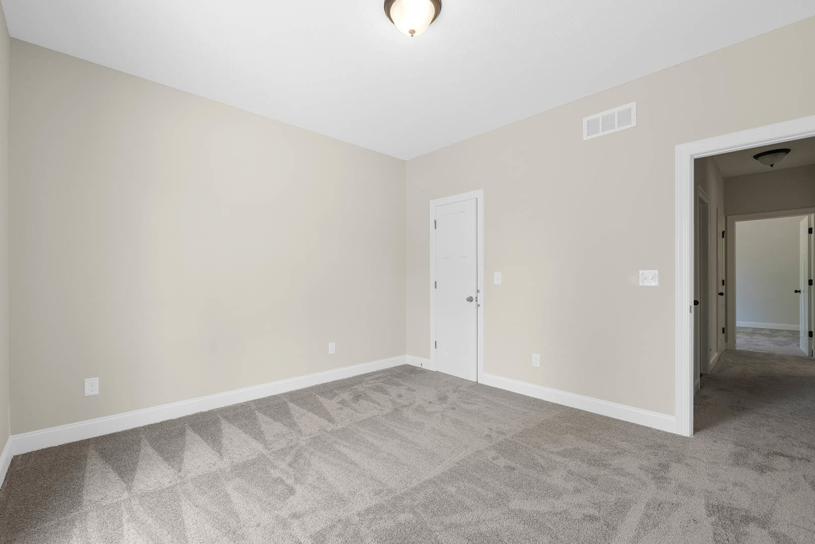 Carpeted room with white walls, white door featuring silver doorknob, white ceiling vent, and close-up of a ceiling light fixture
