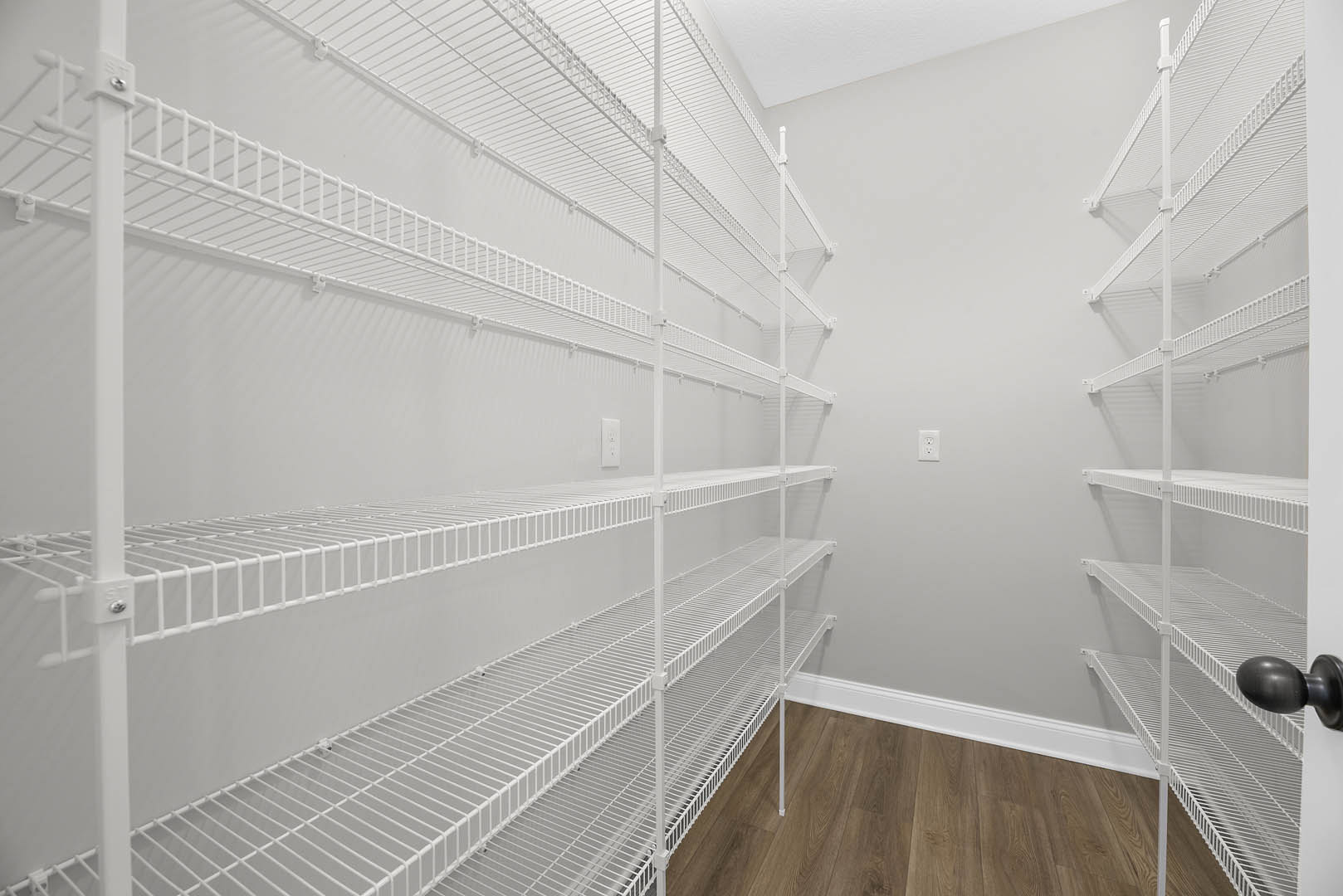 White built-in shelves along a wall, wood flooring with white baseboards, black door knob on a white door