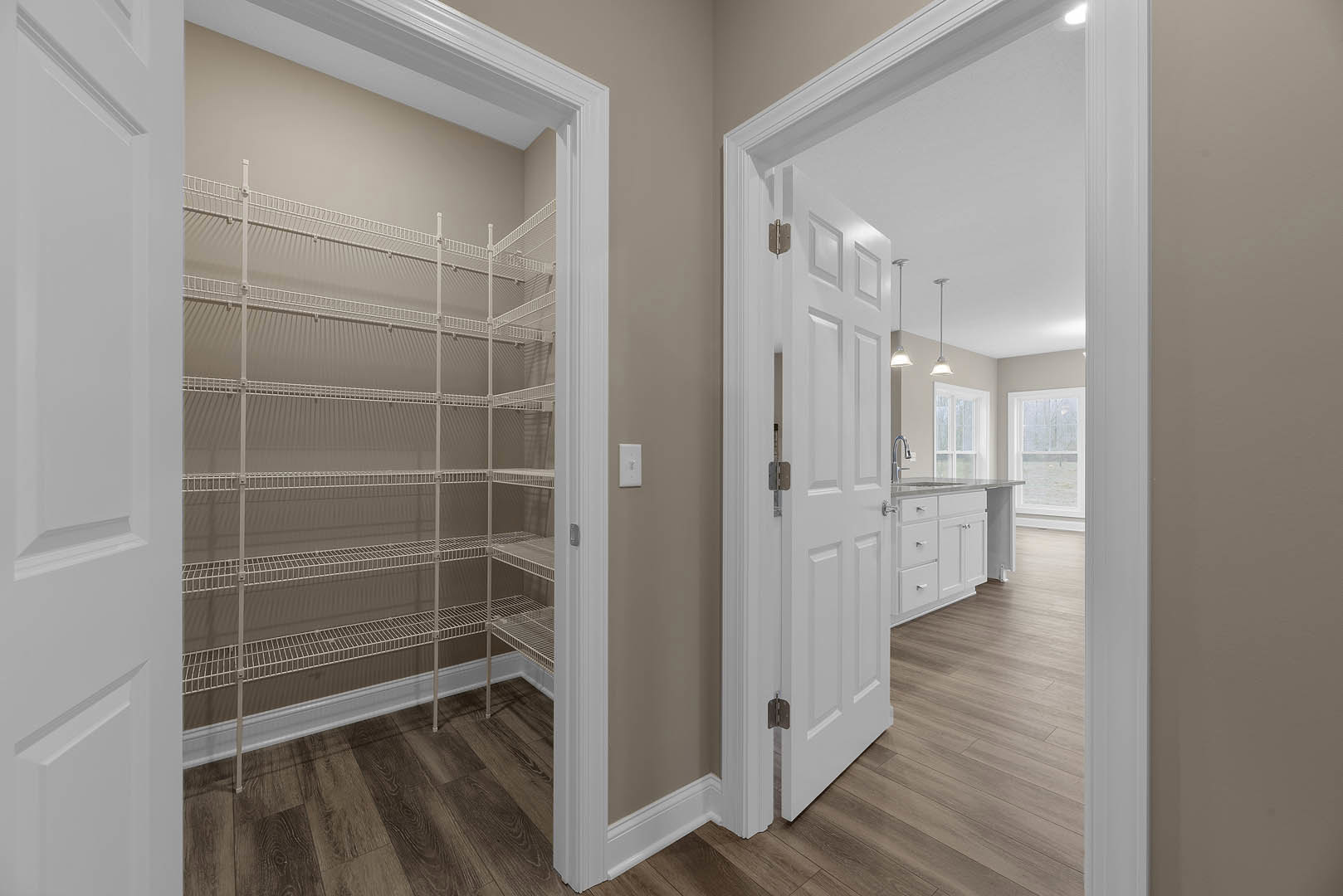 Hallway featuring a white paneled door, built-in white wire shelving, light plaster walls, and hardwood flooring; window offers view of snowy landscape.
