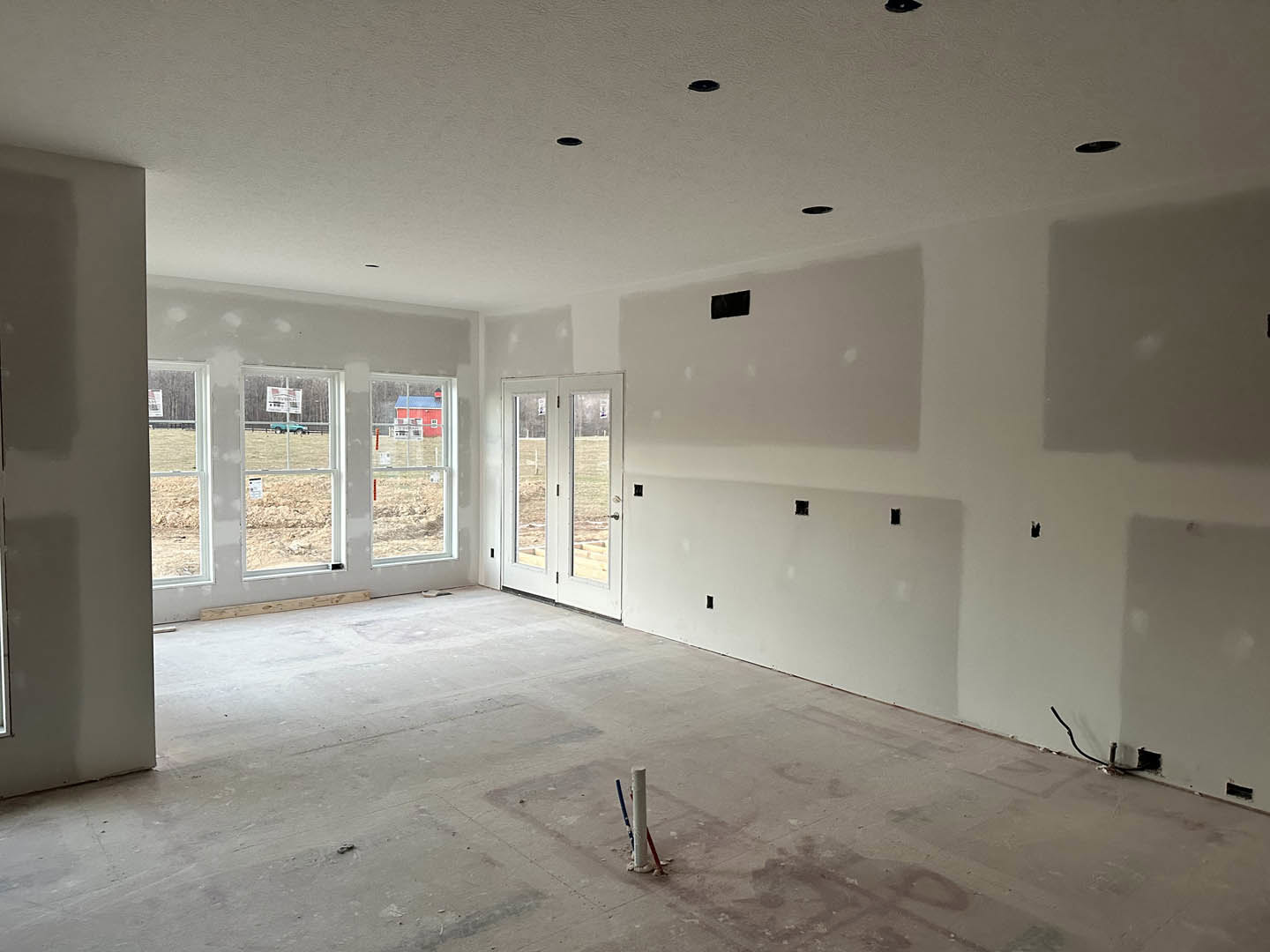 Bright room with smooth white plaster walls, large windows, white door with glass panels, light wood flooring, and view of a red barn through the windows