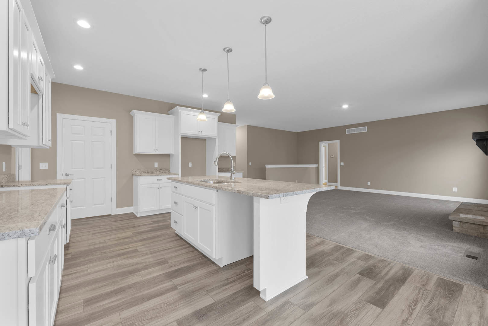 Open-concept kitchen and living room featuring white cabinetry, marble countertops, kitchen island with sink, white door, light switch, and contrasting white and black poles