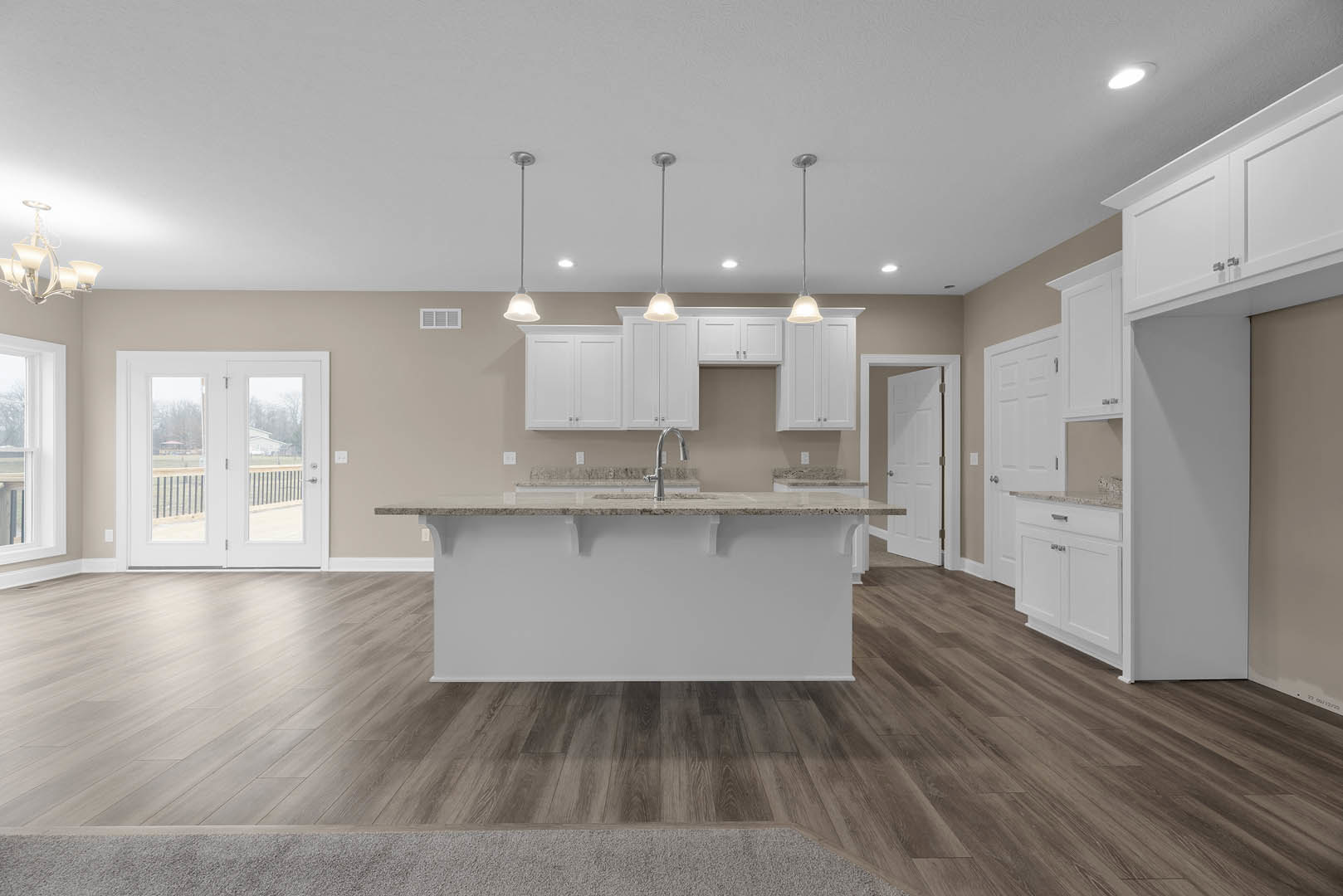 Spacious kitchen featuring a large white island with built-in sink and faucet, wood flooring, white cabinetry, glass-paneled double doors, and ceiling light fixture.