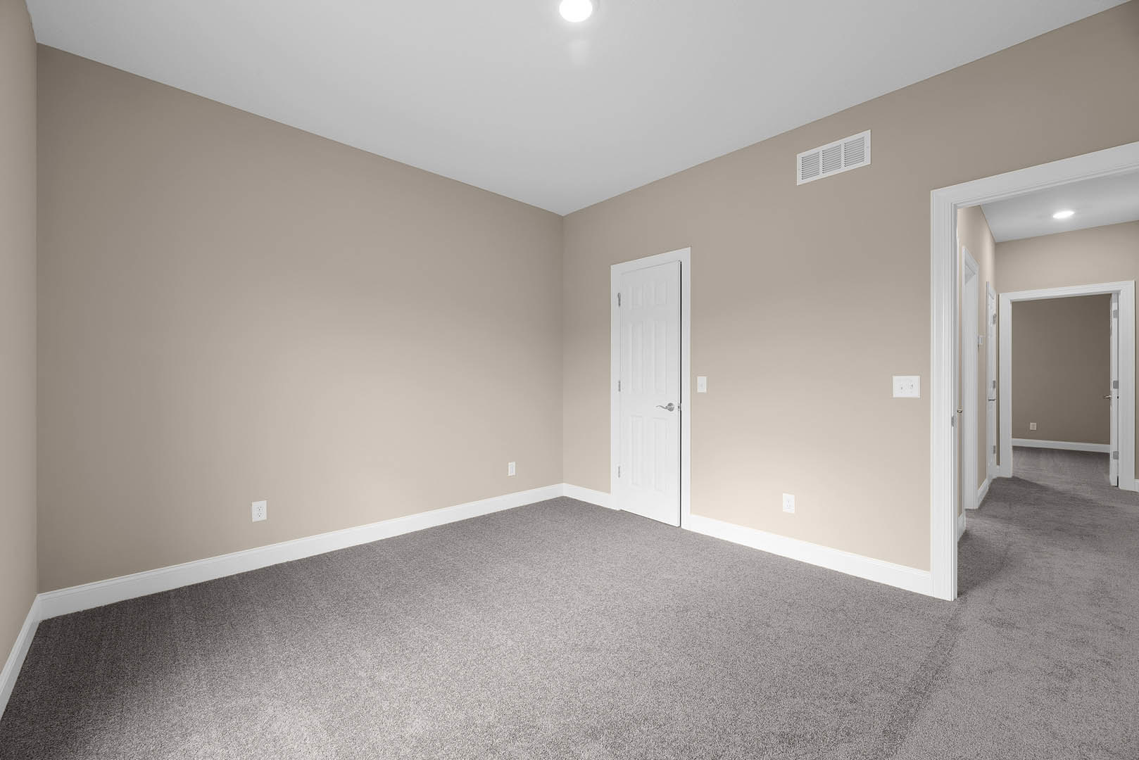 Beige-walled room with white door featuring silver handle, white door frame, carpeted floor, ceiling vent, and simple molding