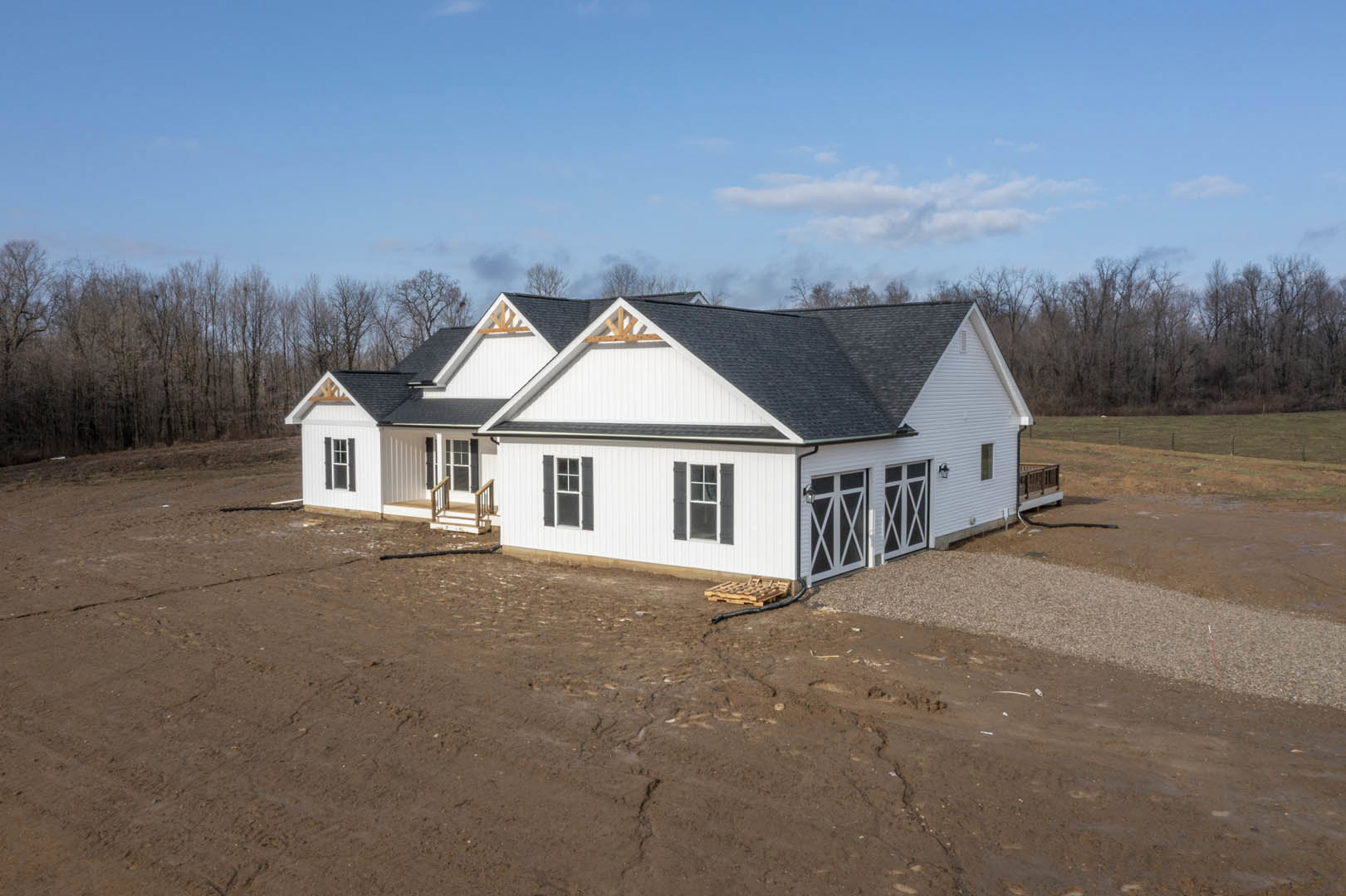 White siding house with attached garage, large dirt yard, white-framed windows, and blue sky with scattered clouds