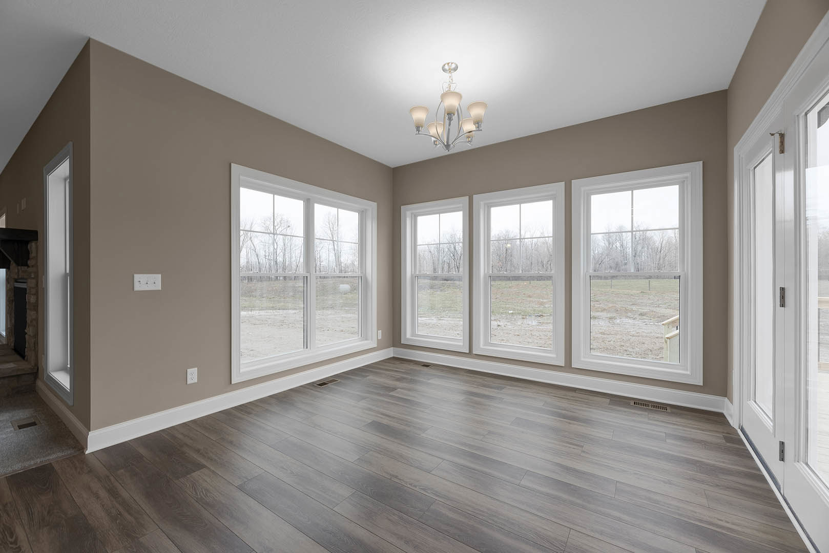 Hardwood floor and large windows overlooking a field and trees, chandelier hanging from ceiling, neutral walls