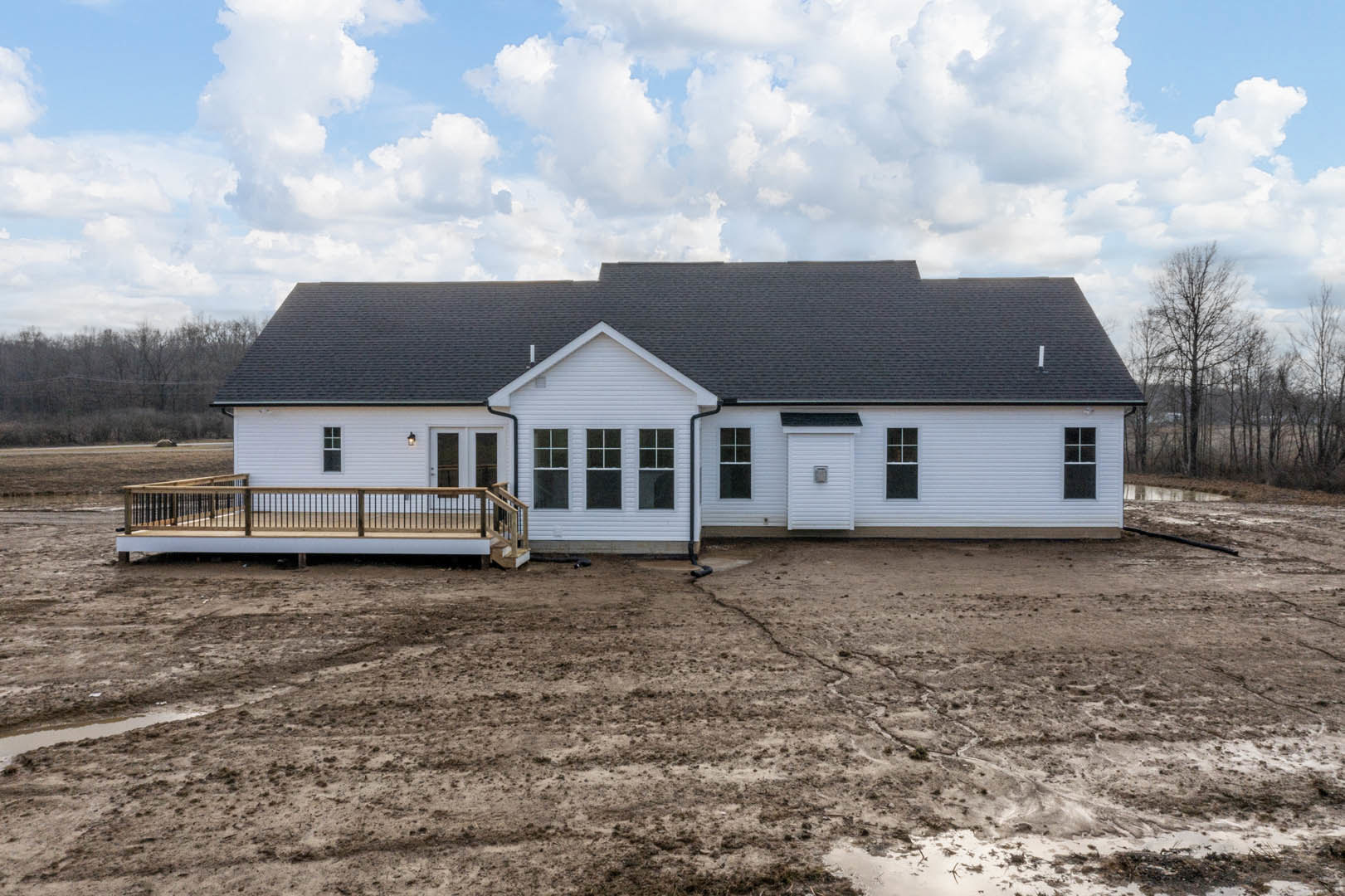 Two-story house with black roof, white siding, elevated deck with metal railing, fenced yard, and porch; cloudy sky overhead.