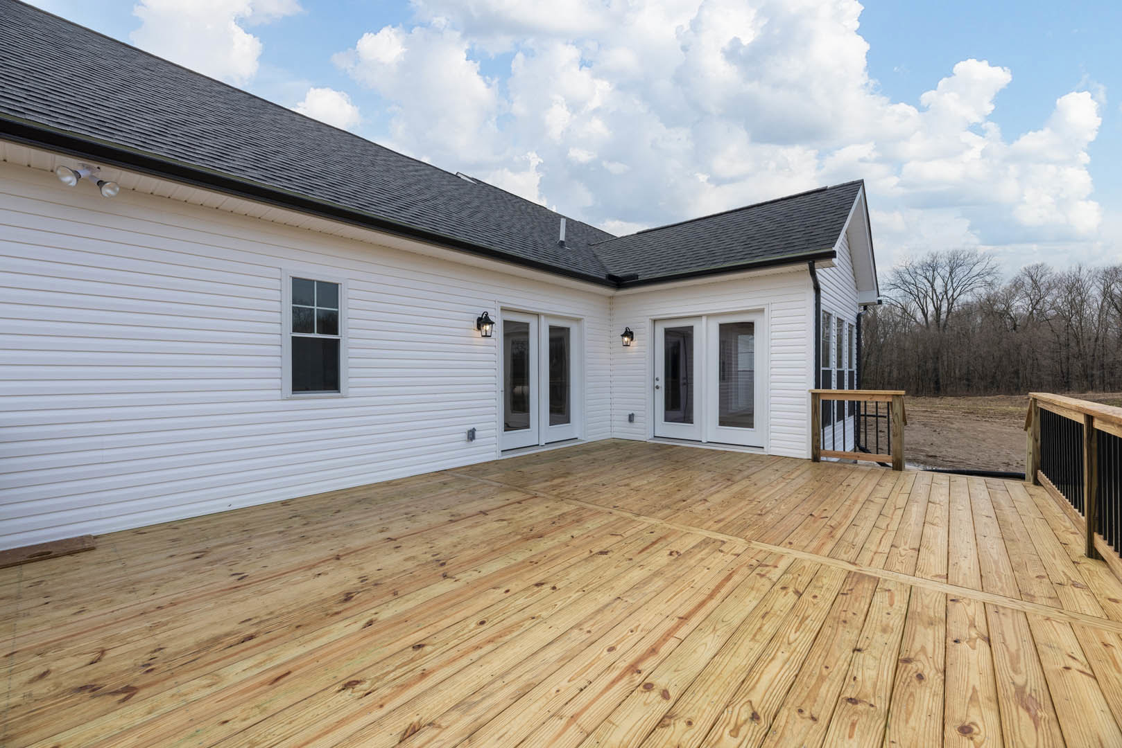 White exterior home with wooden deck, black metal railing, and white-framed window under partly cloudy sky