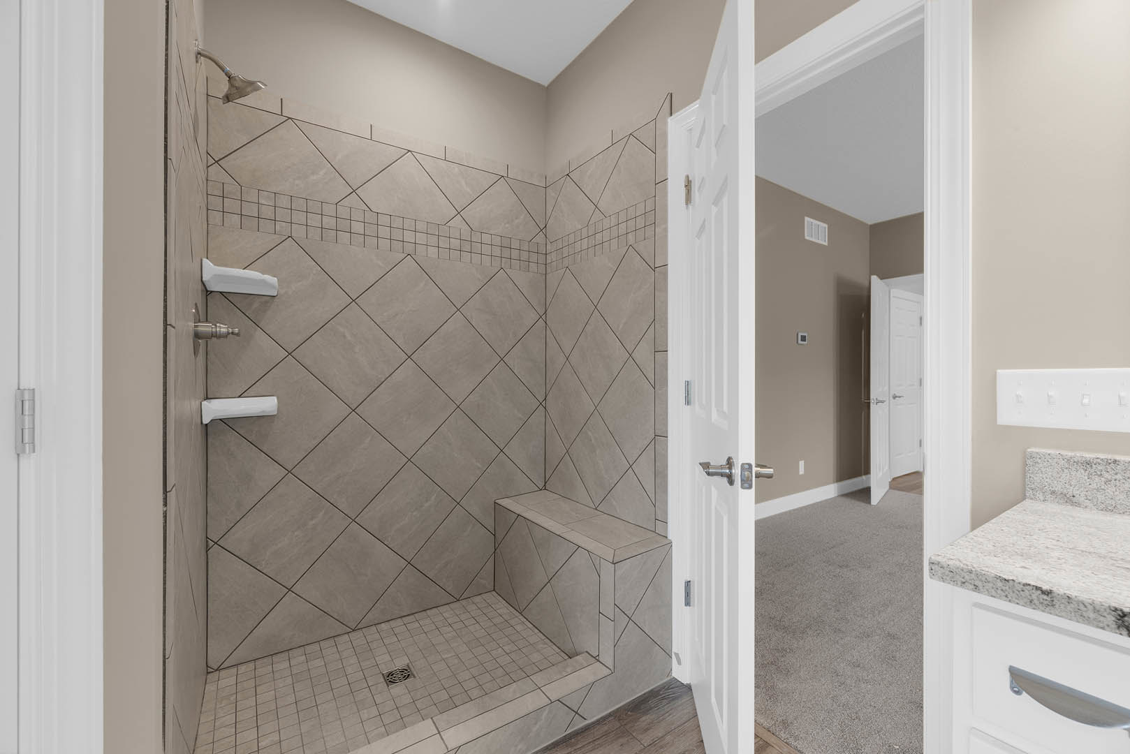 Bathroom with tiled shower featuring built-in bench, white door with silver handles, marble surfaces, and three-switch white light plate