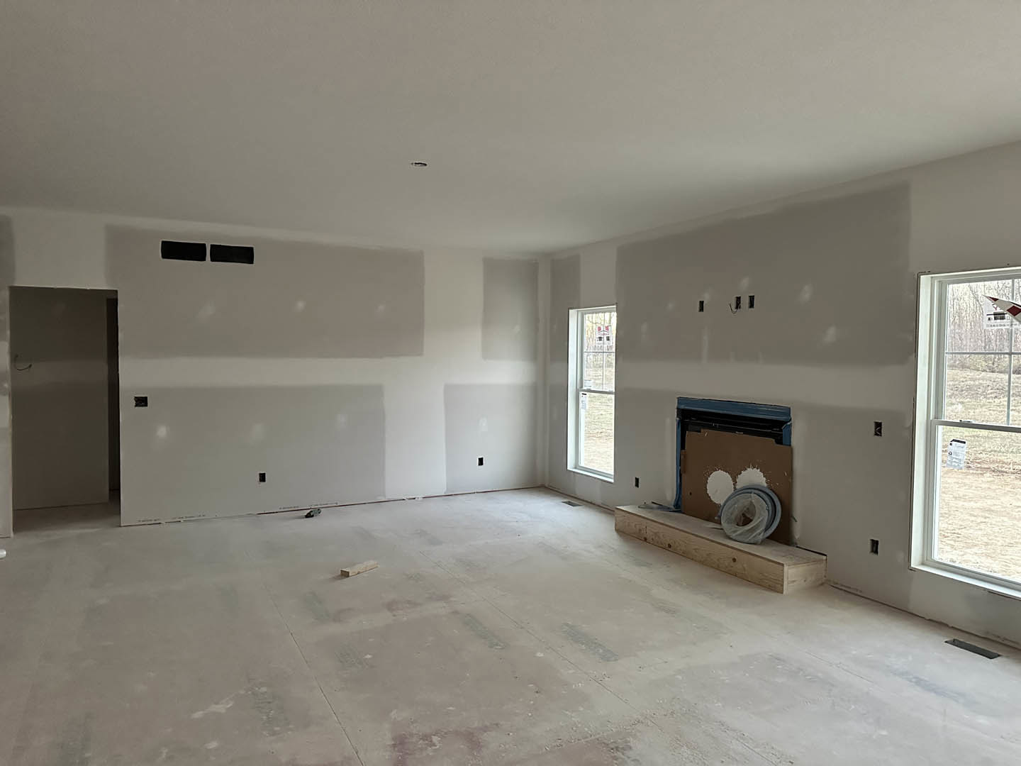 Living room with plaster walls, white-framed window, wood flooring, built-in wood shelf, and modern fireplace.
