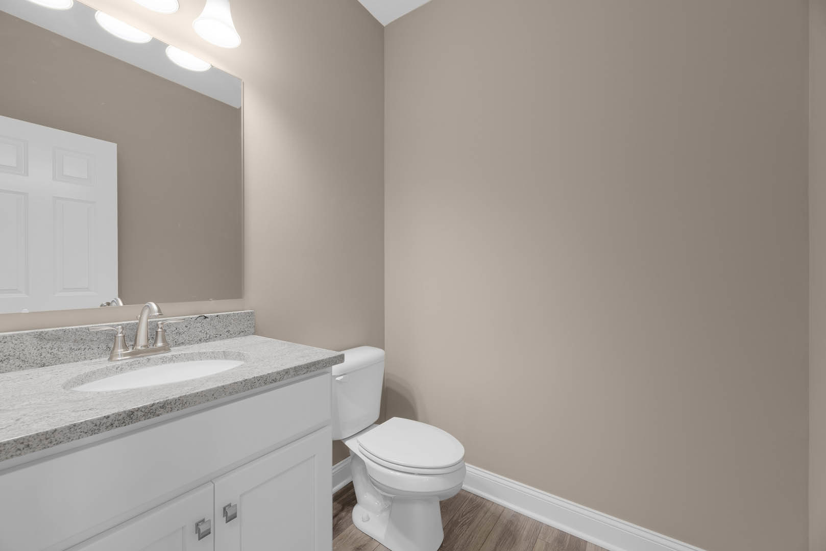 Modern bathroom featuring white ceramic sink and toilet, light gray tile flooring, white paneled door, and partial view of a freestanding bathtub.