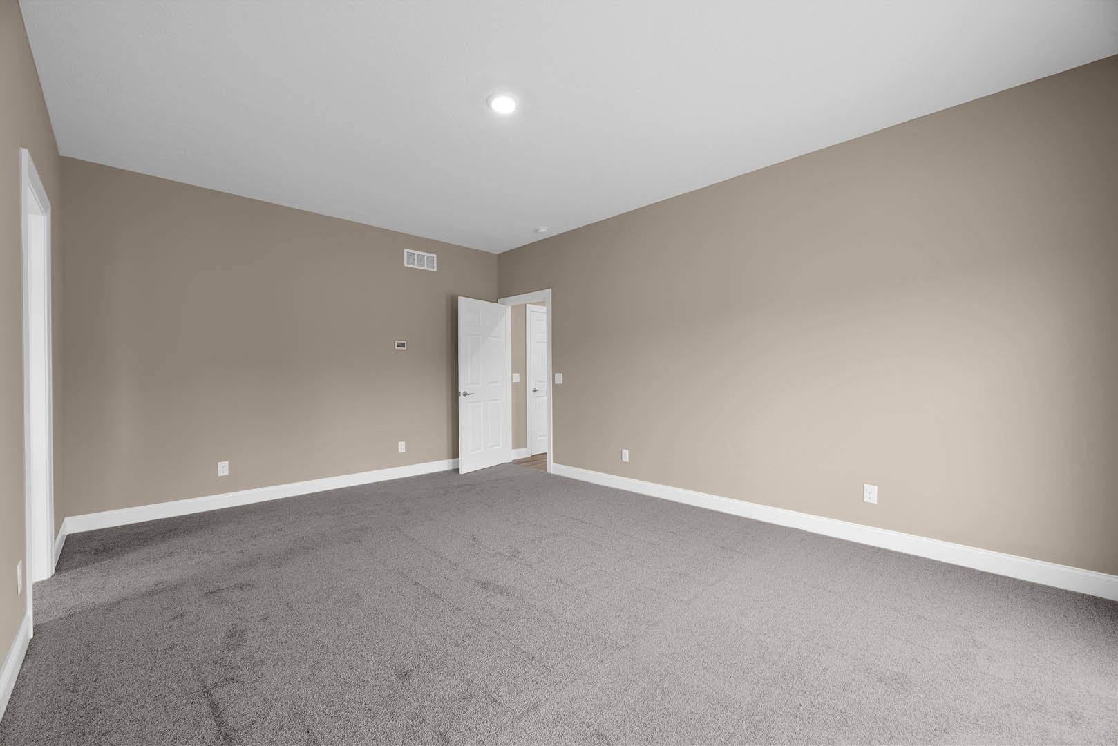 Carpeted room with white door open, silver handle, white walls, ceiling light fixture, empty interior