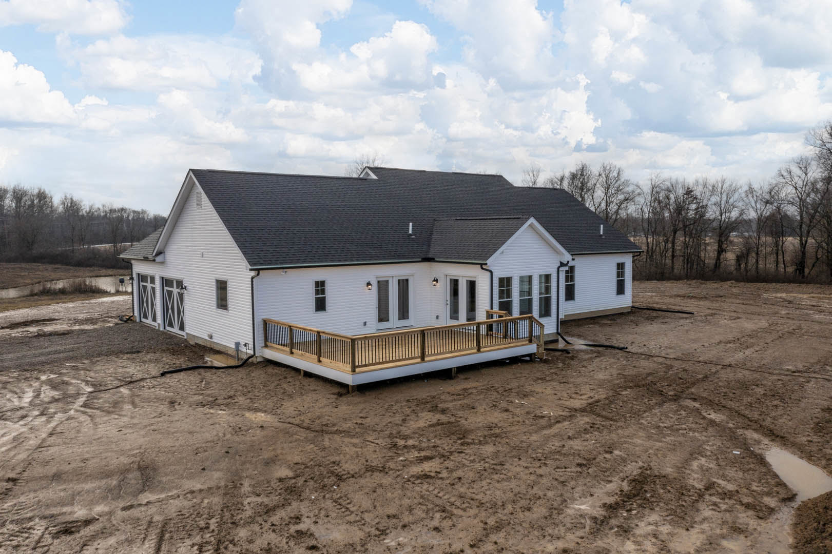 Wood deck with horizontal railing attached to beige siding house, fenced backyard, large windows, gabled roof, partly cloudy sky overhead.