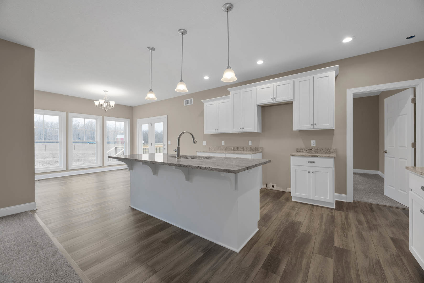Open kitchen and dining area featuring wood flooring, white cabinetry with marble countertops, central island with built-in sink and modern faucet, row of large windows providing