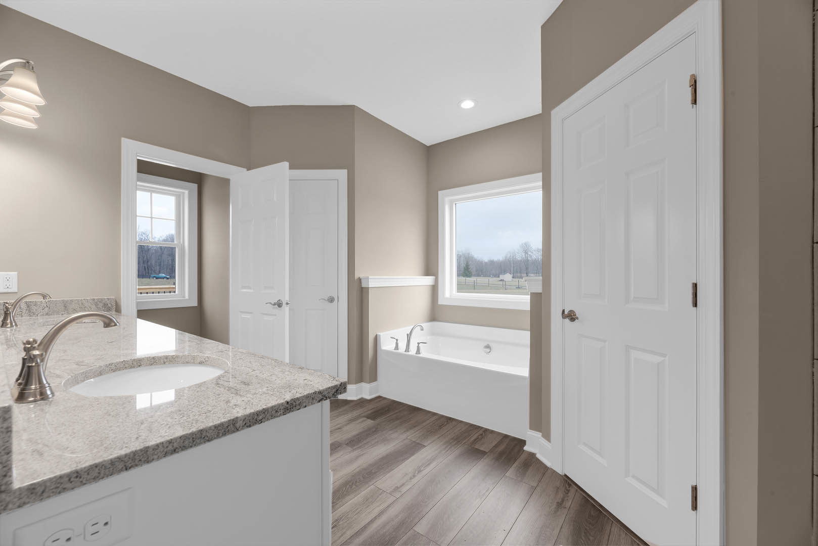 Marble countertop with chrome faucet beside freestanding bathtub, white cabinetry, tile flooring, and window overlooking field and trees