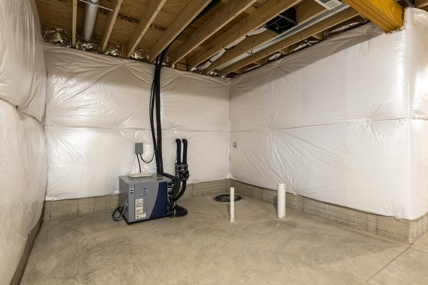 White plaster wall, grey metal box with blue and black handle, exposed wooden ceiling beam, white pipe on concrete floor, white pole with black text.