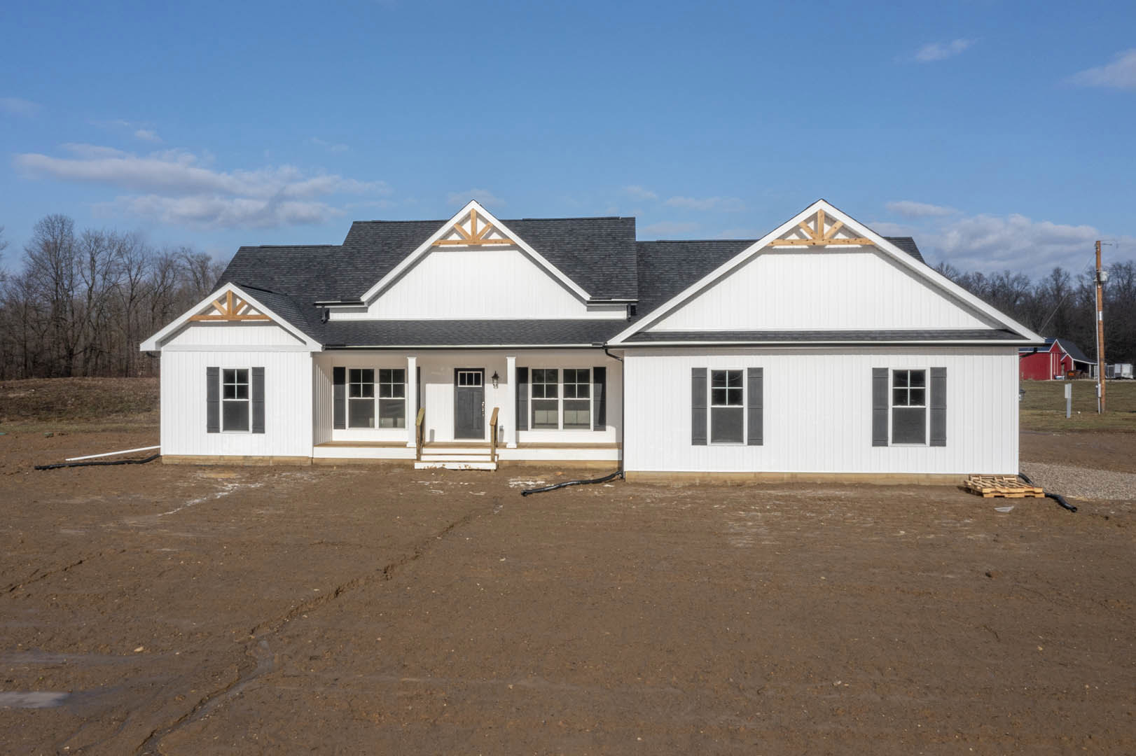 White house with multi-pane windows, white frames, pitched roof, dirt yard in front, trees and cloudy sky in background