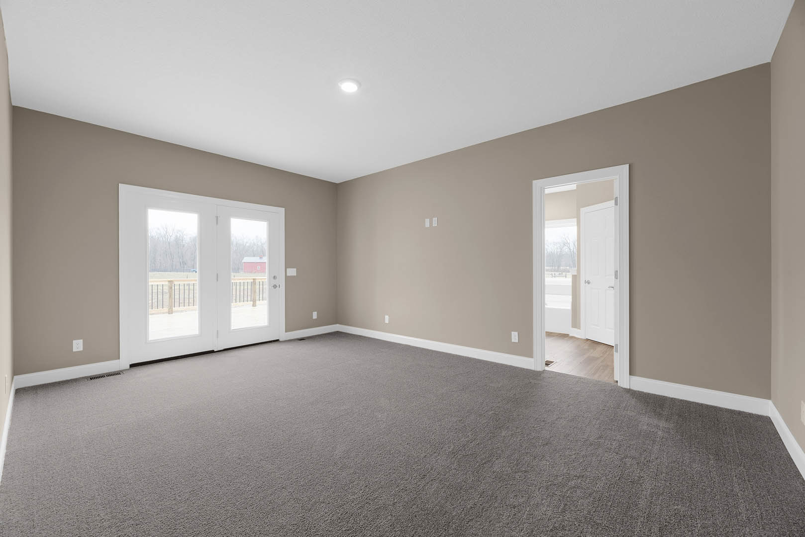 Double glass doors open to a balcony with snowy landscape views, grey carpet flooring, white walls, ceiling light fixture, and decorative molding.