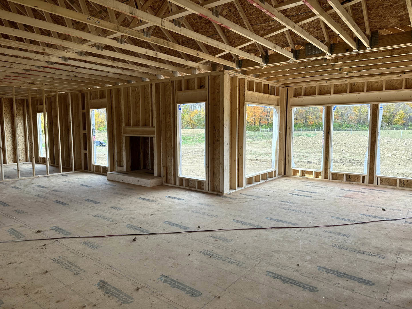 Spacious room with large windows, exposed wood beam ceiling, hardwood floors, and a wire lying across the floor; window overlooks grassy field.
